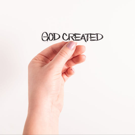 Hand with pink nail polish on a white background with 'GOD CREATED' text.
