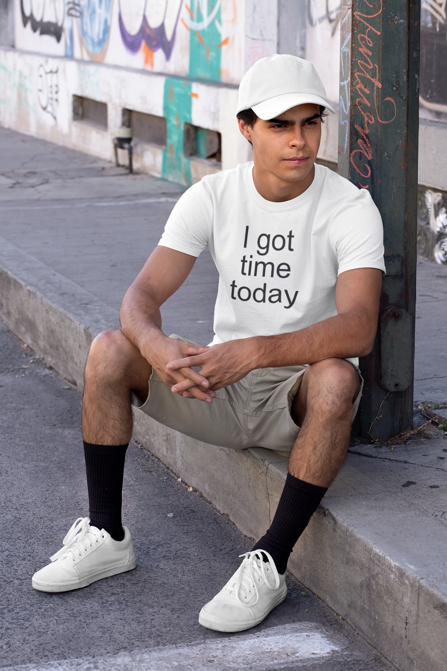 Person wearing a white t-shirt with 'I got time today' text, sitting on a sidewalk.